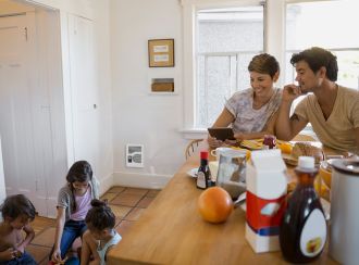 Parents watching their children play on the kitchen floor with the Cadet Energy Plus heater on the wall behind them