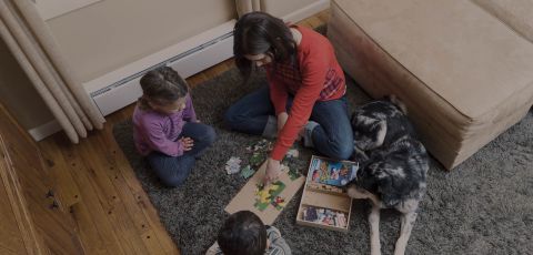 A mother building a jigsaw with two children and a dog