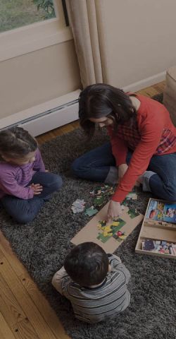 A mother building a jigsaw with two children and a dog